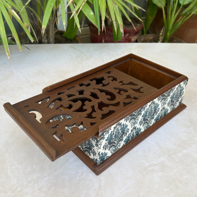 Decorative wooden box with intricate carvings on a light surface, plants in the background.