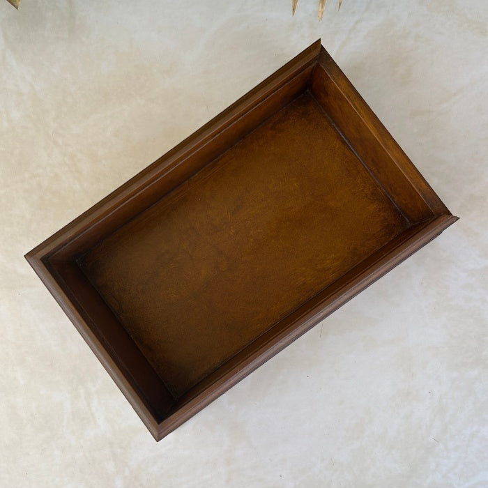 Inside of wooden box on a textured surface with green leaves in the background