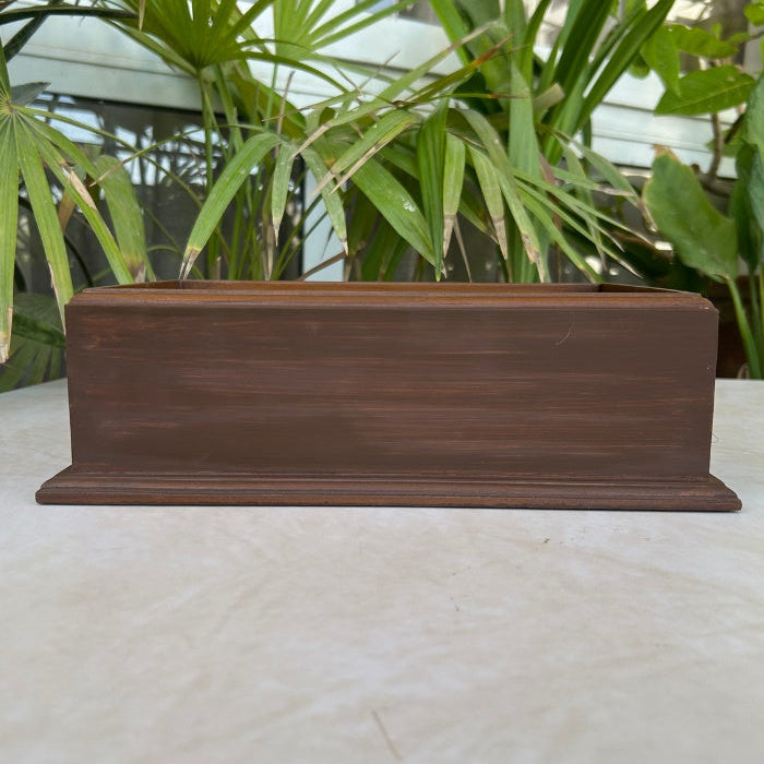 Wooden box on a light surface with green plants in the background