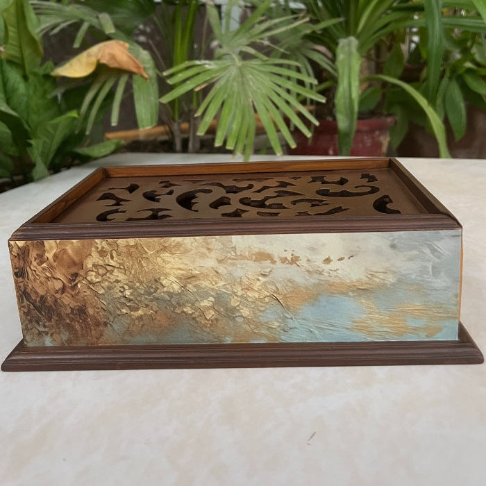 Decorative metal box with intricate design on a surface with plants in the background