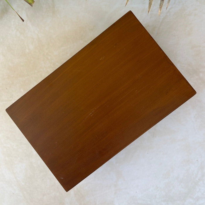 Bottom view of wooden box on a textured surface with green leaves in the background