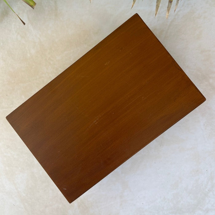Bottom view of wooden box on a textured surface with green leaves in the background