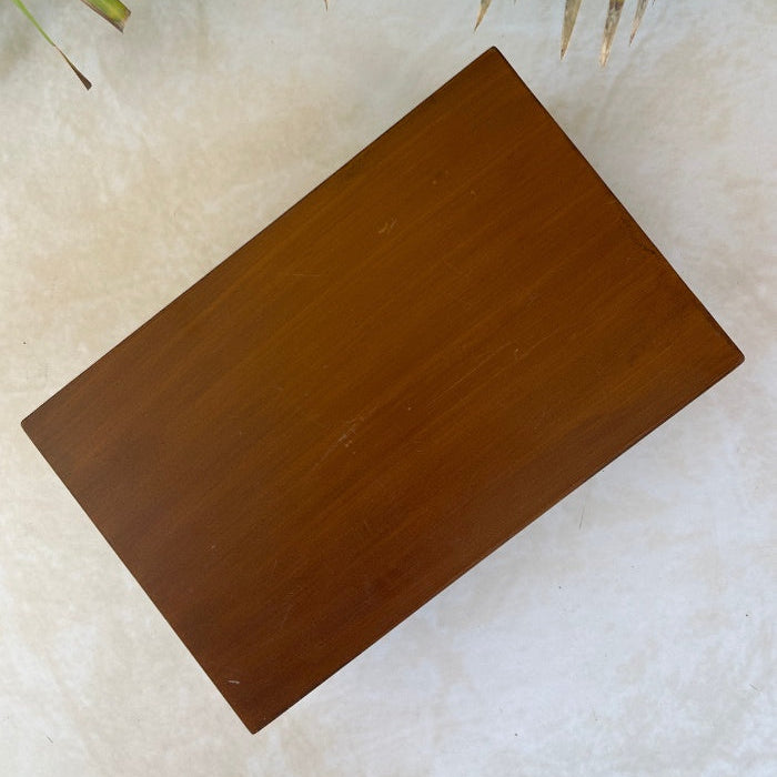 Wooden box on a textured surface with green leaves in the background