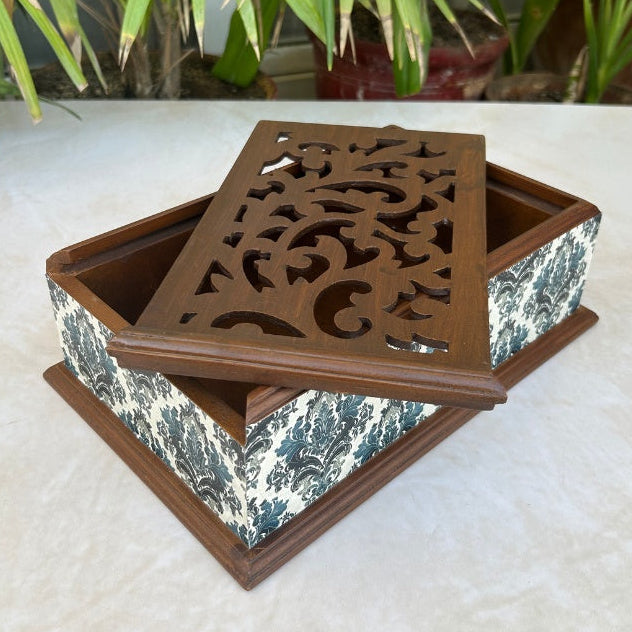 Decorative wooden box with intricate carvings on a light surface with plants in the background