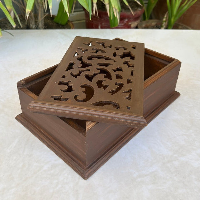 Wooden decorative box with intricate carvings on a white surface with plants in the background