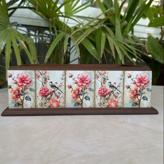 Decorative box with floral and bird design on a surface with plants in the background