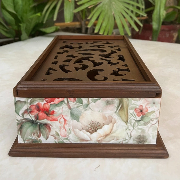 Wooden box with floral design on a white surface with plants in the background