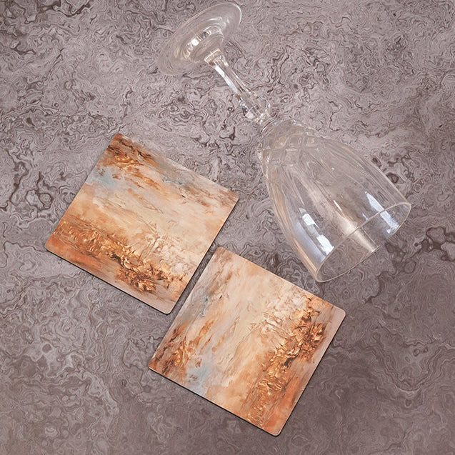 Two glass coasters with a rustic design on a gray textured surface.